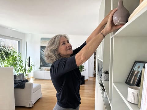 Best-Ager-Frau greift mühelos in ein hohes Regal, gelöste Schultern und freier Nacken im Alltag